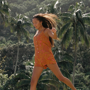 woman with brown hair wearing an orange tie back romper with puakenikeni print