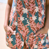 woman with brown hair wearing a blue thin strap tie back romper with red ginger and tiare print. 