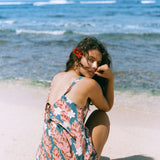 woman with brown hair wearing a blue thin strap tie back romper with red ginger and tiare print. 