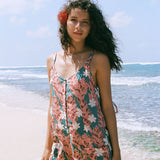 woman with brown hair wearing a blue thin strap tie back romper with red ginger and tiare print. 