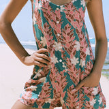 woman with brown hair wearing a thin strap tie back romper with red ginger and tiare print. 