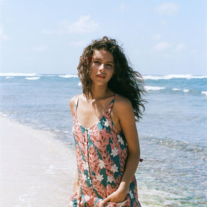 woman with brown hair wearing a blue thin strap tie back romper with red ginger and tiare print. 