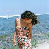 woman with brown hair wearing a blue thin strap tie back romper with red ginger and tiare print. 