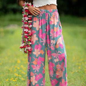 woman with brown hair wearing teal flowy pants with orange and pink foral print