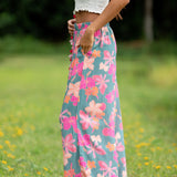 woman with brown hair wearing teal flowy pants with orange and pink foral print