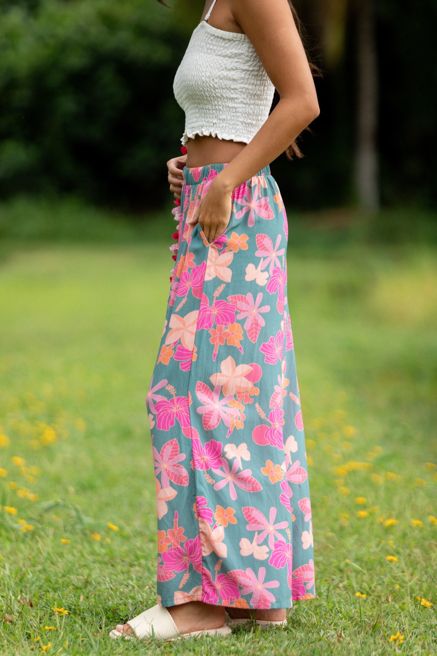woman with brown hair wearing teal flowy pants with orange and pink foral print