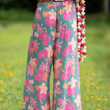 woman with brown hair wearing teal flowy pants with orange and pink foral print