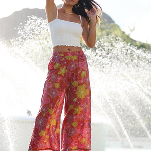 woman wearing terracotta colored pants with large purple and yellow flower print