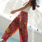 woman wearing terracotta colored pants with large purple and yellow flower print