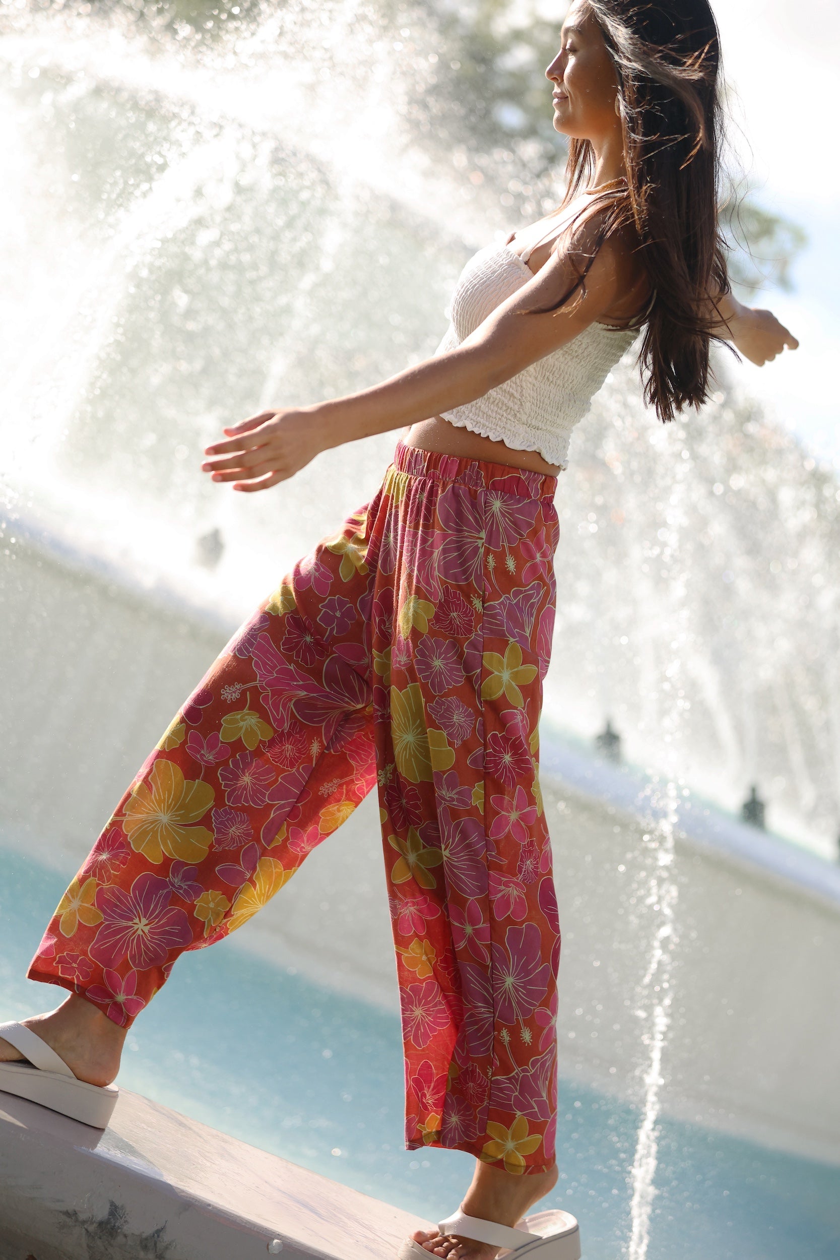 woman wearing terracotta colored pants with large purple and yellow flower print