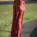 woman wearing terracotta colored pants with large purple and yellow flower print