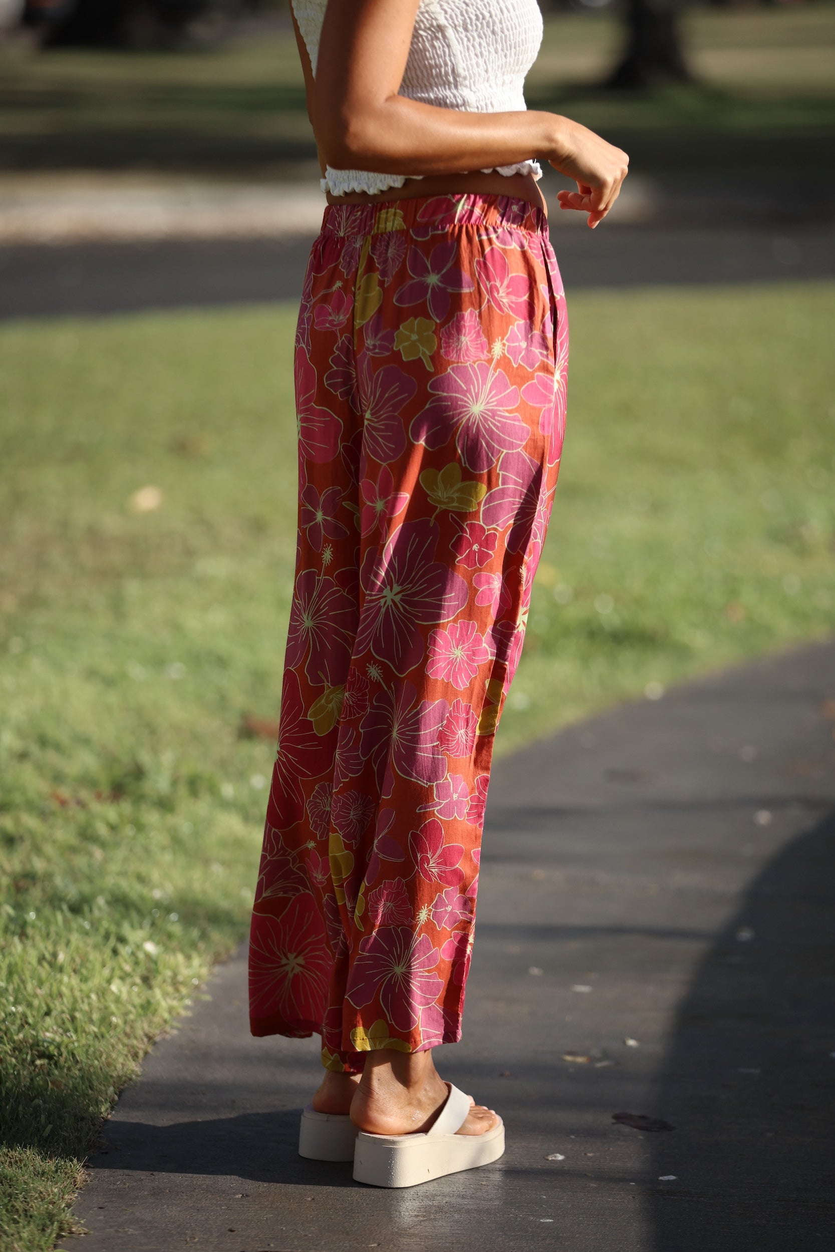 woman wearing terracotta colored pants with large purple and yellow flower print