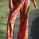 woman wearing terracotta colored pants with large purple and yellow flower print