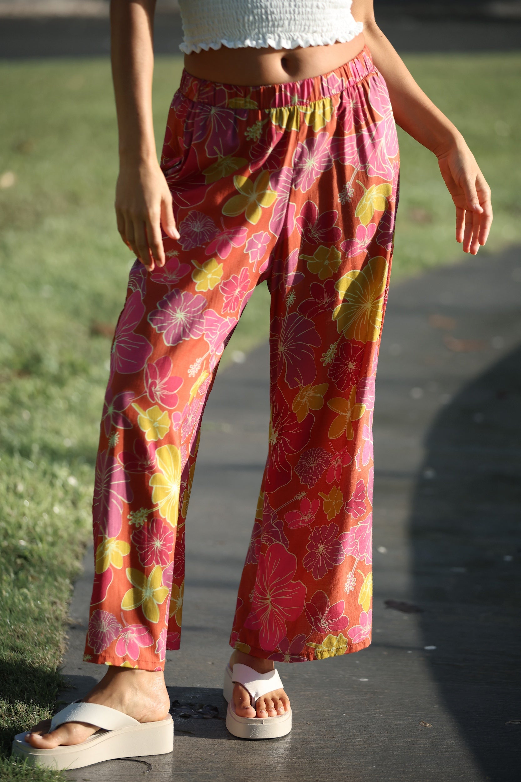 woman wearing terracotta colored pants with large purple and yellow flower print