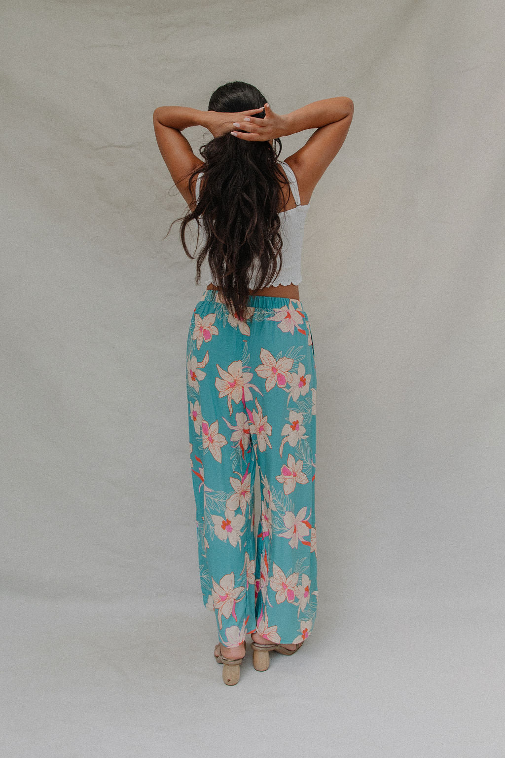 woman with brown hair wearing teal flowy pants with white orchid pattern