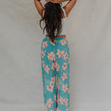 woman with brown hair wearing teal flowy pants with white orchid pattern