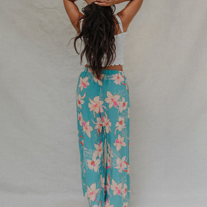 woman with brown hair wearing teal flowy pants with white orchid pattern
