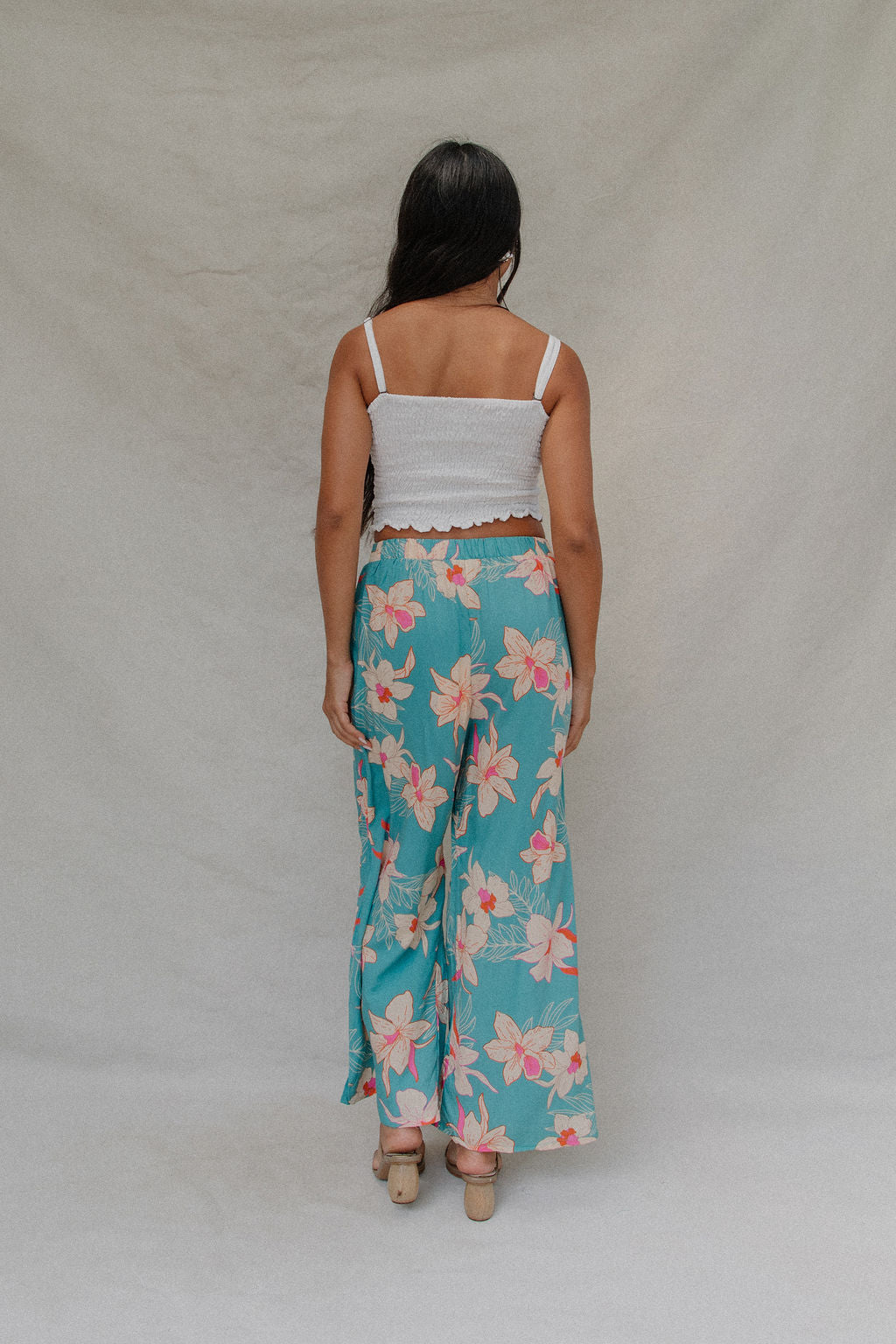 woman with brown hair wearing teal flowy pants with white orchid pattern