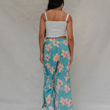 woman with brown hair wearing teal flowy pants with white orchid pattern