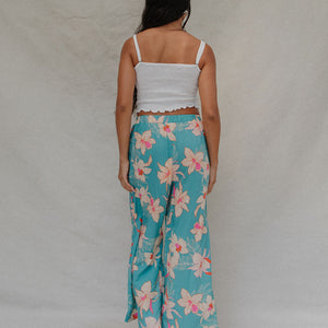 woman with brown hair wearing teal flowy pants with white orchid pattern