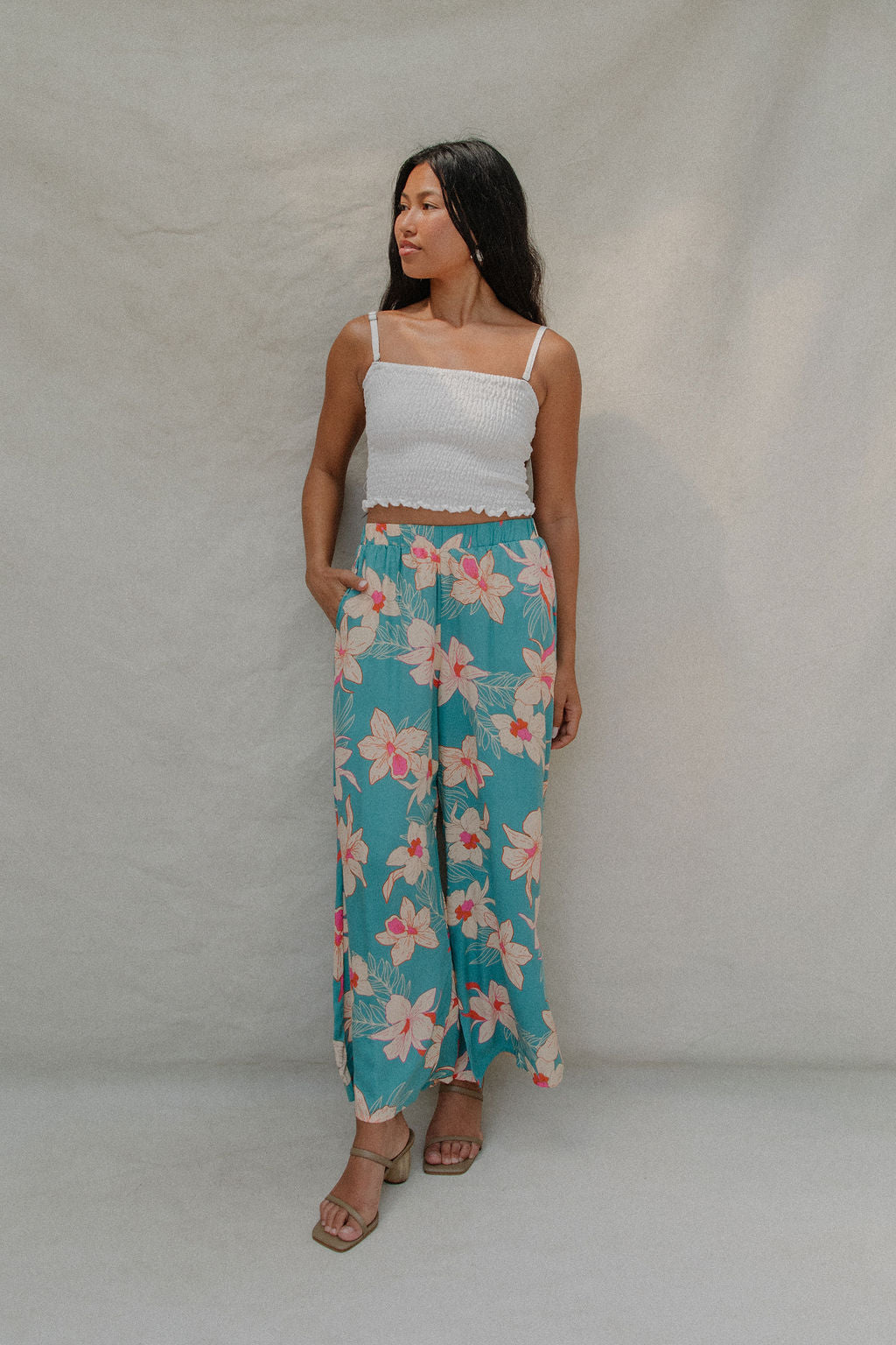 woman with brown hair wearing teal flowy pants with white orchid pattern