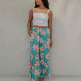 woman with brown hair wearing teal flowy pants with white orchid pattern