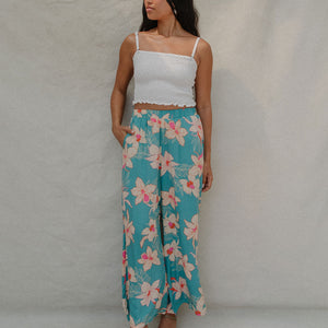 woman with brown hair wearing teal flowy pants with white orchid pattern