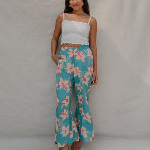 woman with brown hair wearing teal flowy pants with white orchid pattern