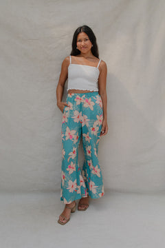 woman with brown hair wearing teal flowy pants with white orchid pattern