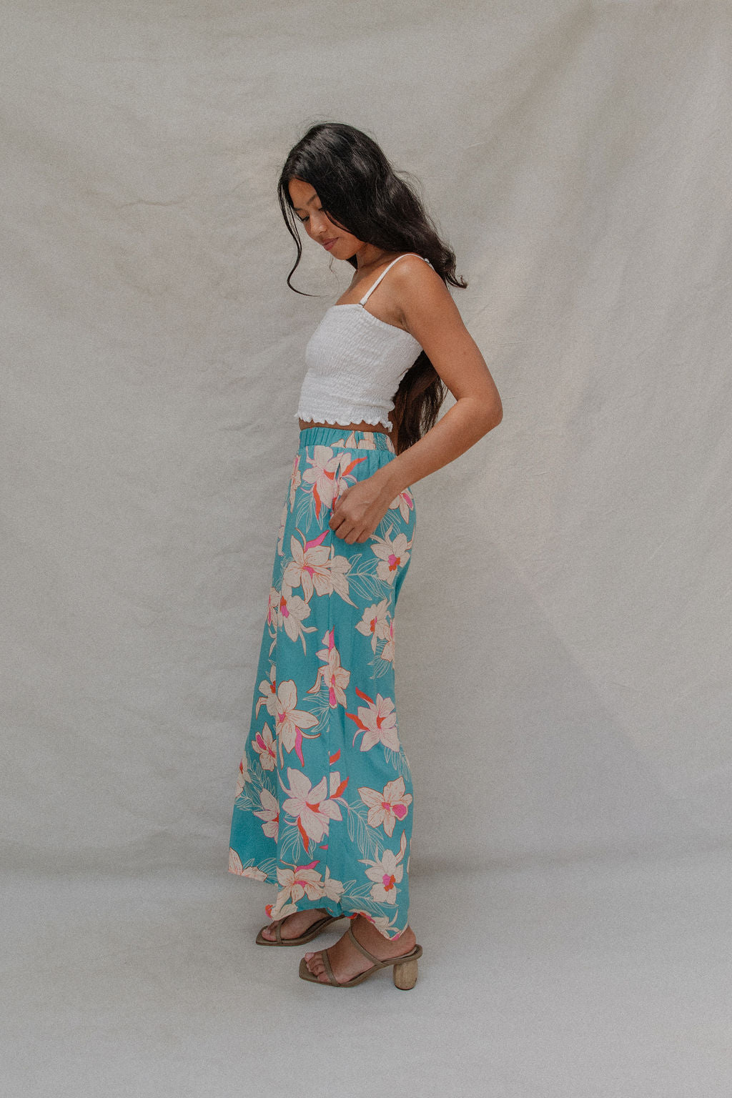 woman with brown hair wearing teal flowy pants with white orchid pattern