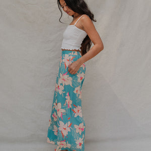 woman with brown hair wearing teal flowy pants with white orchid pattern