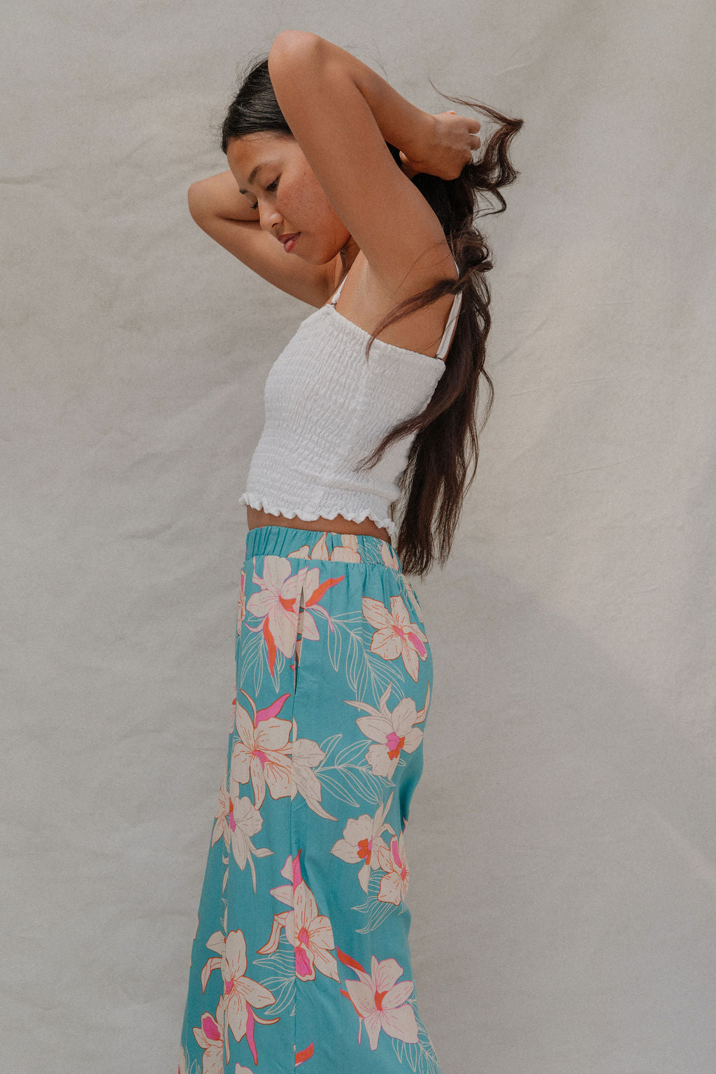 woman with brown hair wearing teal flowy pants with white orchid pattern