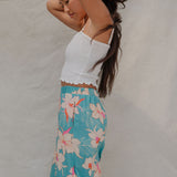 woman with brown hair wearing teal flowy pants with white orchid pattern