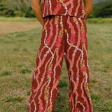 woman with brown hair wearing red-brown colored pant and top with button closure back and lei print