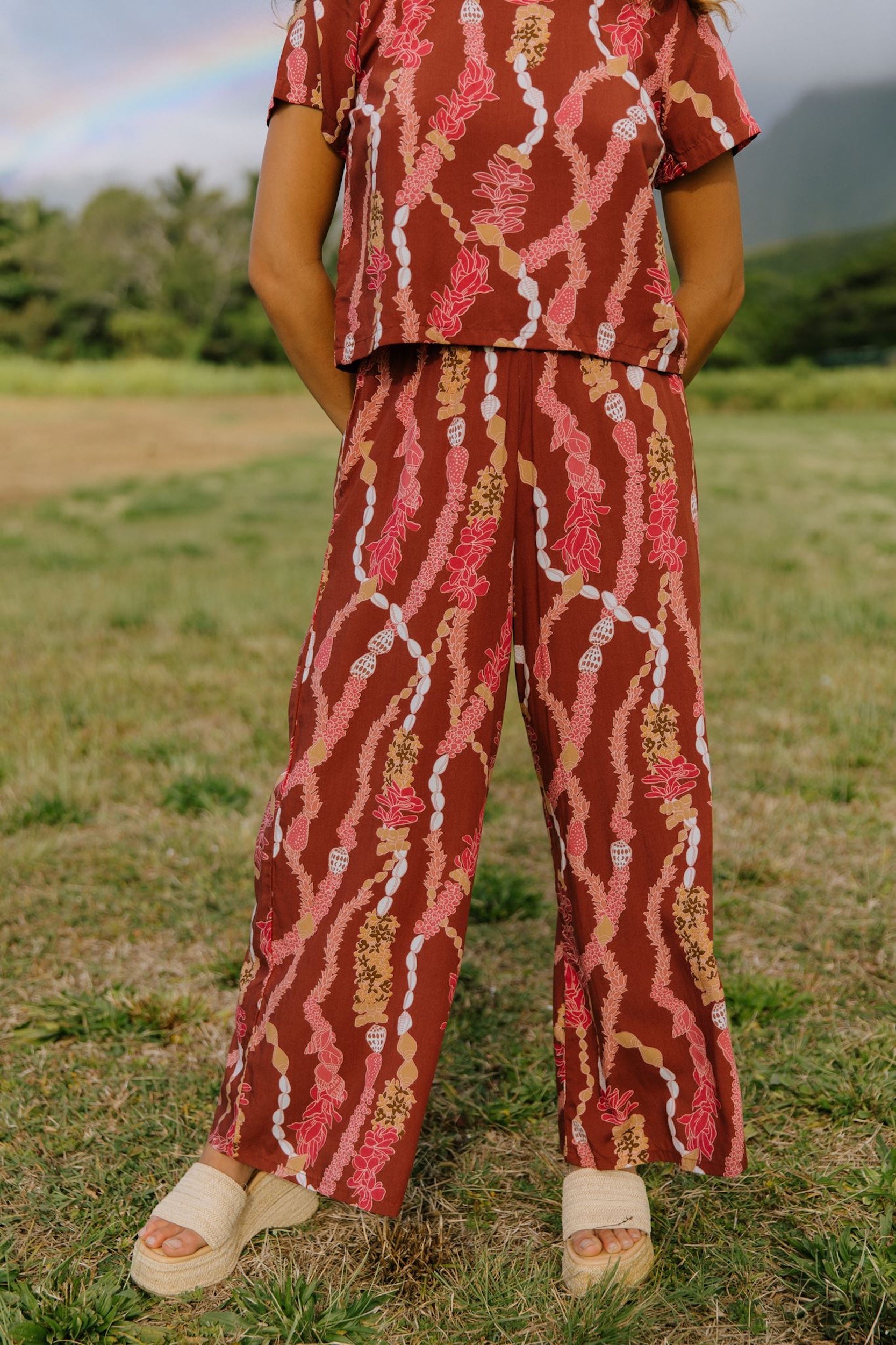 woman with brown hair wearing red-brown colored pant and top with button closure back and lei print