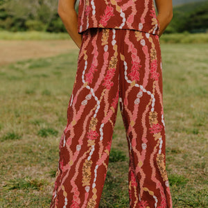 woman with brown hair wearing red-brown colored pant and top with button closure back and lei print