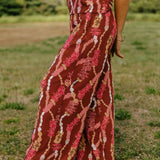 woman with brown hair wearing red-brown colored pant and top with button closure back and lei print