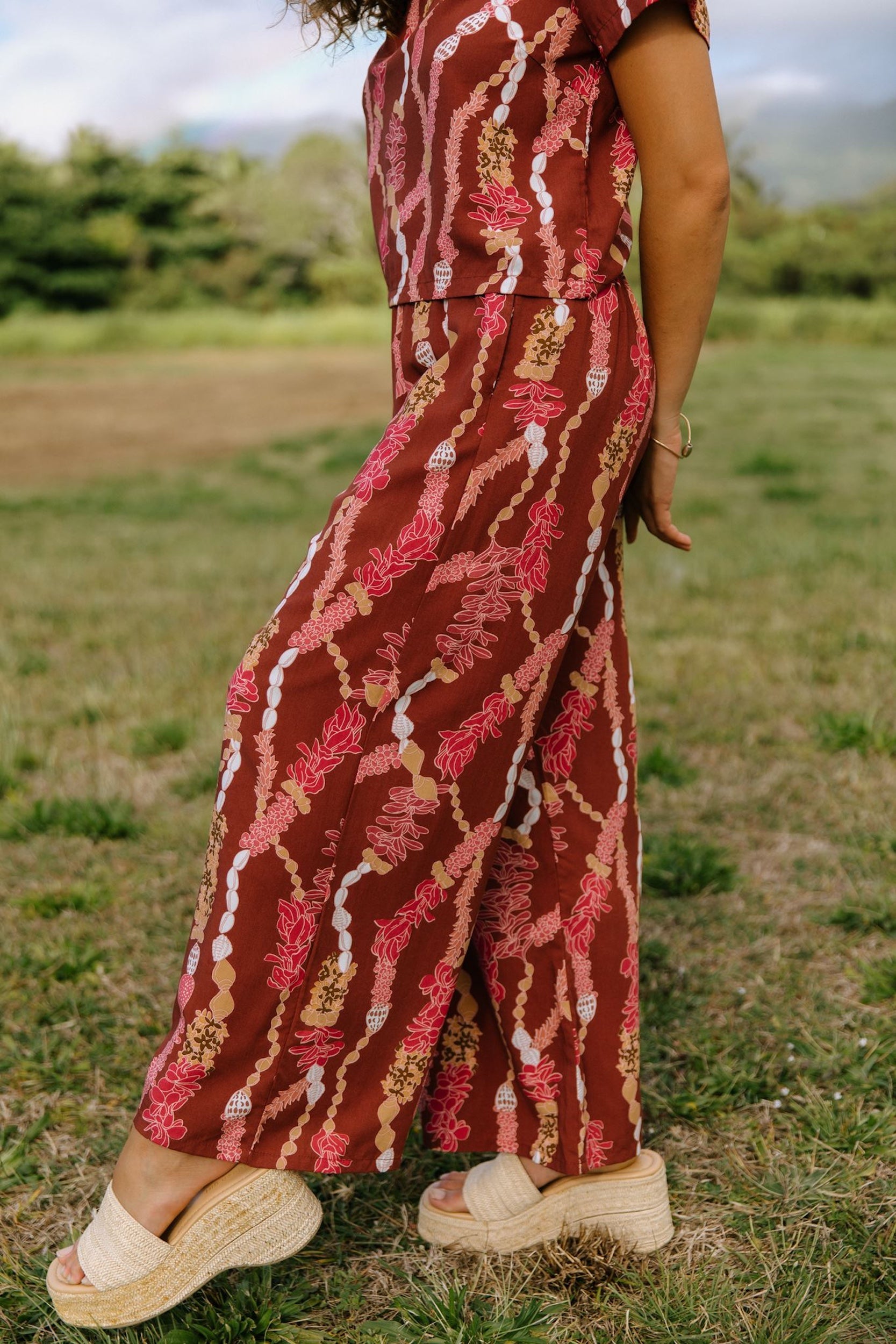 woman with brown hair wearing red-brown colored pant and top with button closure back and lei print