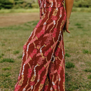woman with brown hair wearing red-brown colored pant and top with button closure back and lei print