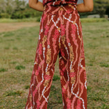 woman with brown hair wearing red-brown colored pant and top with button closure back and lei print