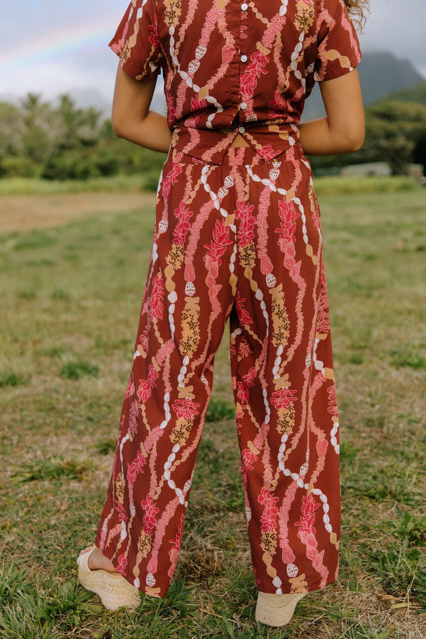 woman with brown hair wearing red-brown colored pant and top with button closure back and lei print