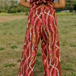 woman with brown hair wearing red-brown colored pant and top with button closure back and lei print
