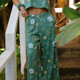 woman wearing lush green long flowy pants with puakenikeni