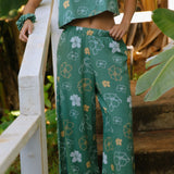 woman wearing lush green long flowy pants with puakenikeni