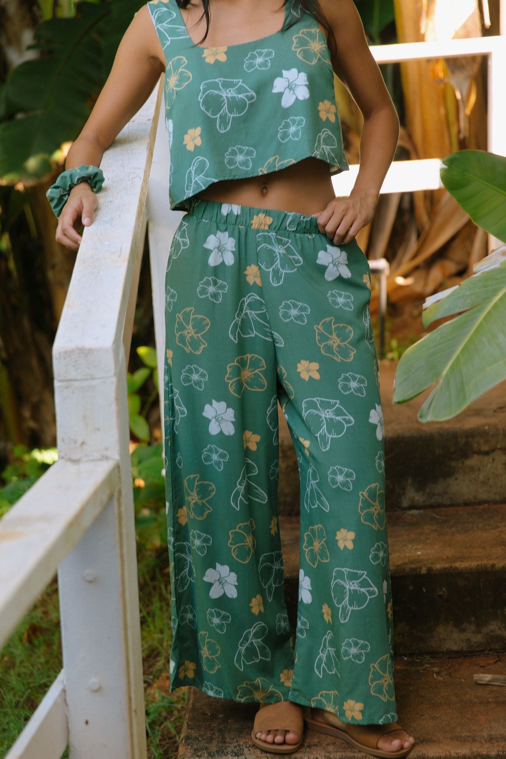 woman wearing lush green long flowy pants with puakenikeni