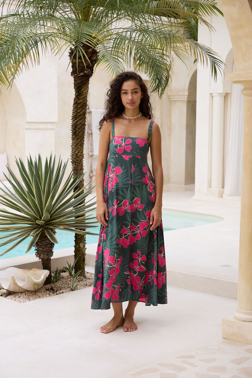 woman with brown hair wearing a dark green thin strap dress with fern and ginger print
