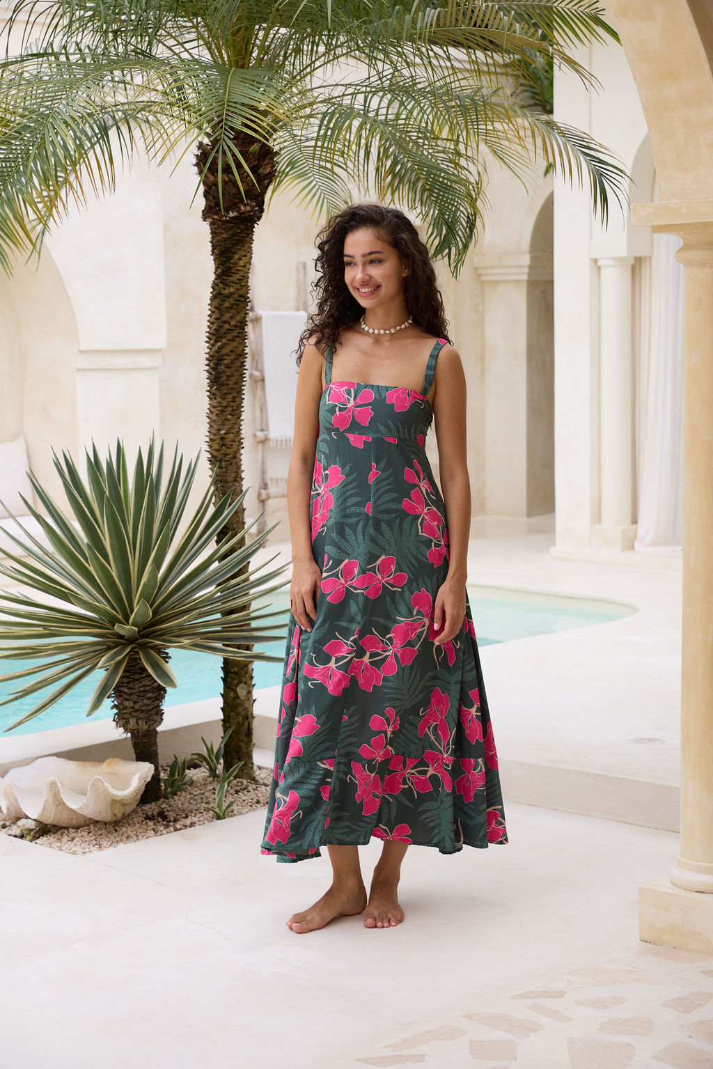 woman with brown hair wearing a dark green thin strap dress with fern and ginger print