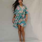 woman with brown hair wearing a teal puff sleeve dress with white orchid pattern