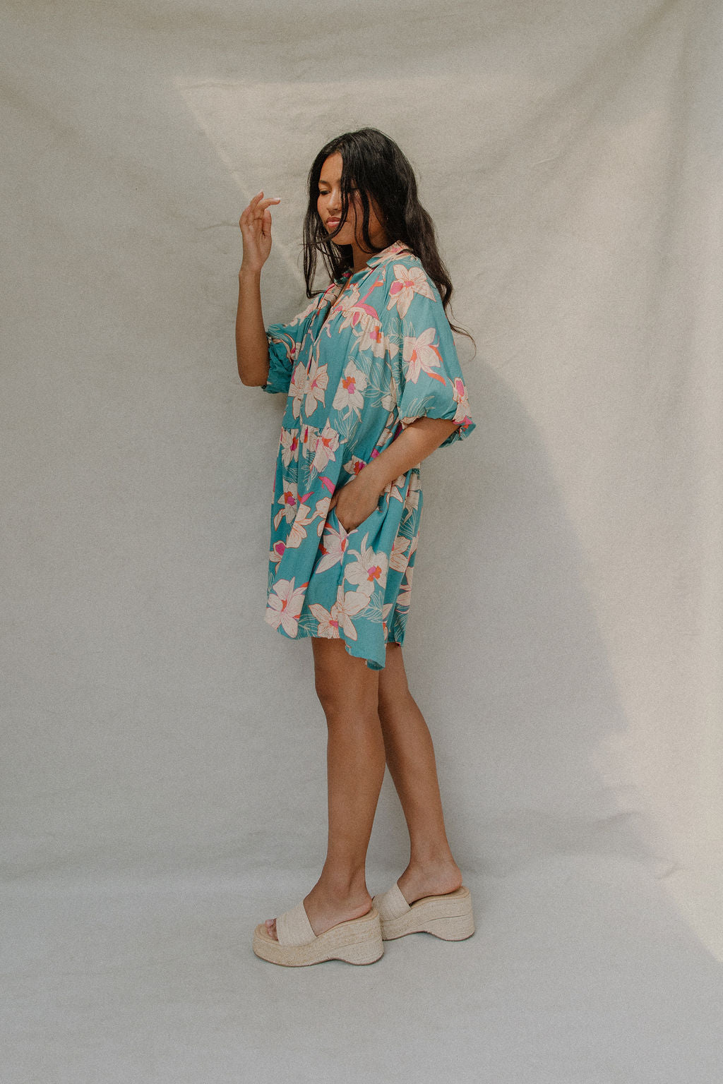 woman with brown hair wearing a teal puff sleeve dress with white orchid pattern