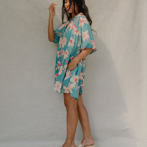 woman with brown hair wearing a teal puff sleeve dress with white orchid pattern